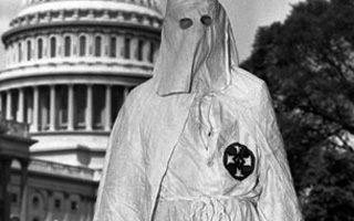 Man in KKK hood and robes. U.S. capitol building can be seen in the background.