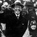 President Woodrow Wilson holding a baseball in a crowd filled outdoor stadium.